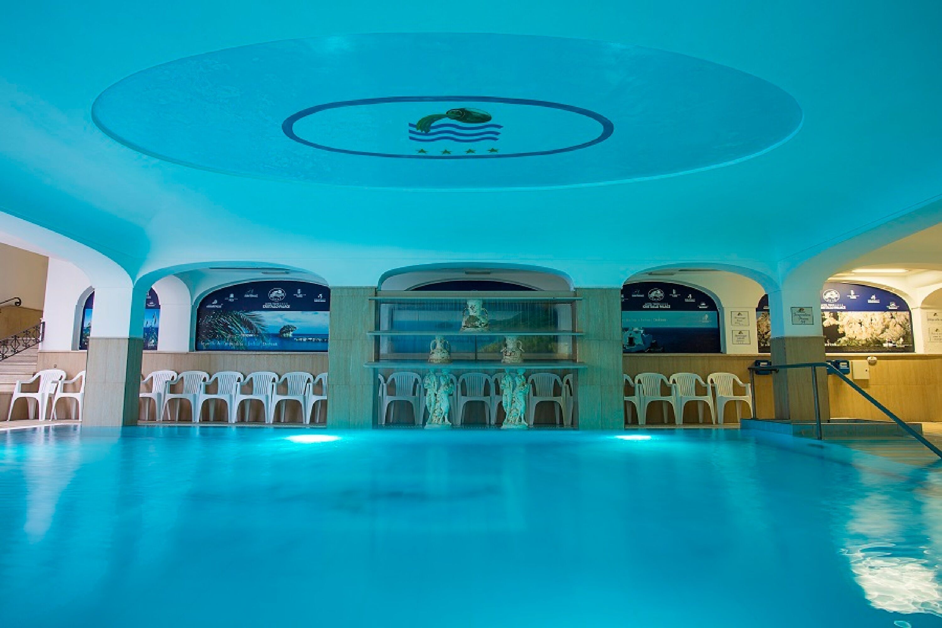 A swimming pool with a central statue, seating areas, and a ceiling with a circular design.