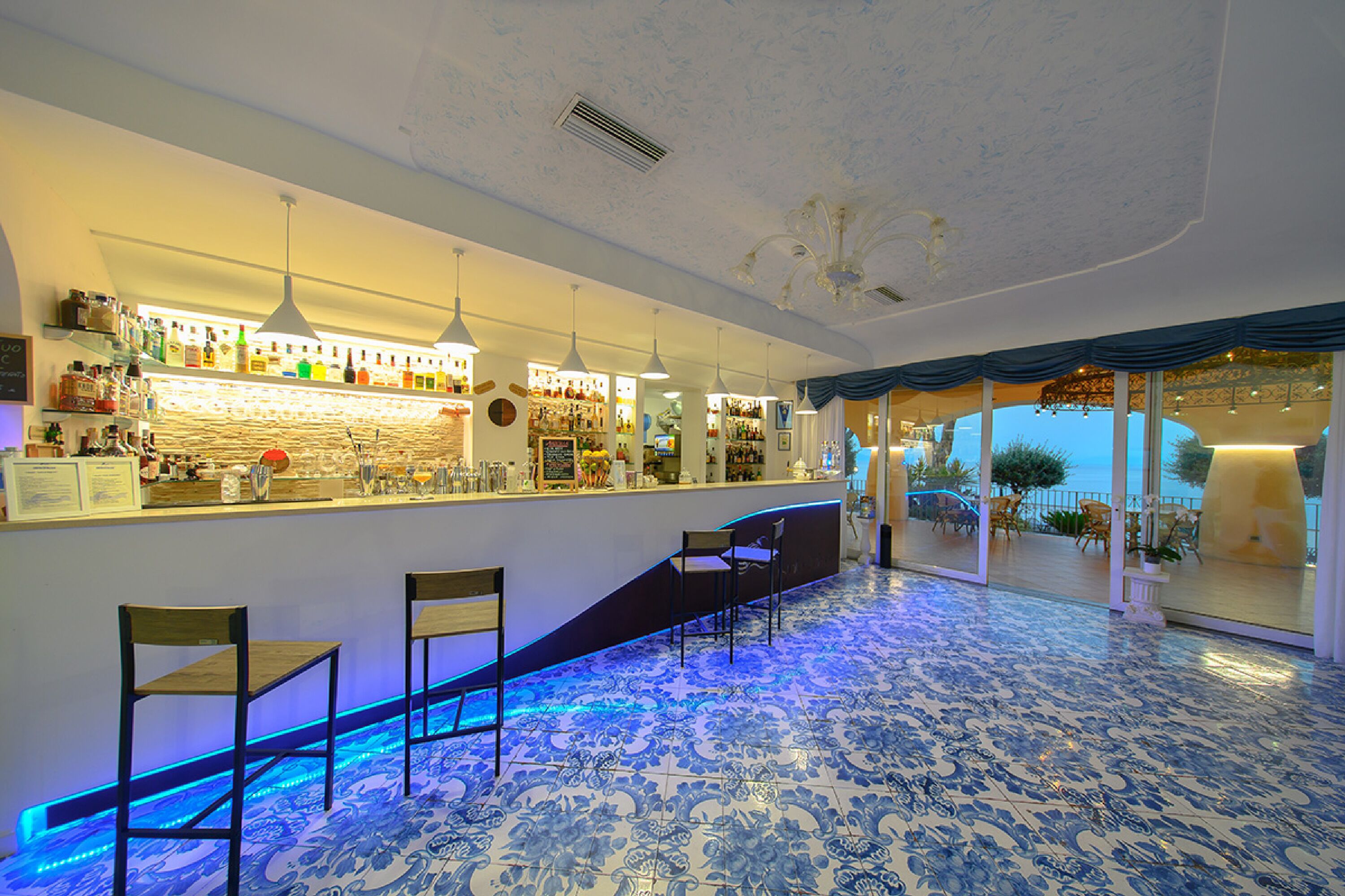 Eine Bar mit Theke, Barhocker und Meerblick durch große Fenster.