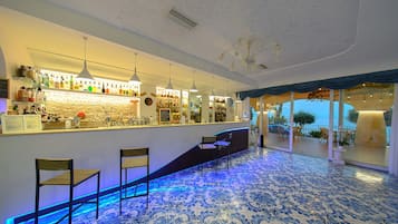 Eine Bar mit Theke, Barhocker und Meerblick durch große Fenster.