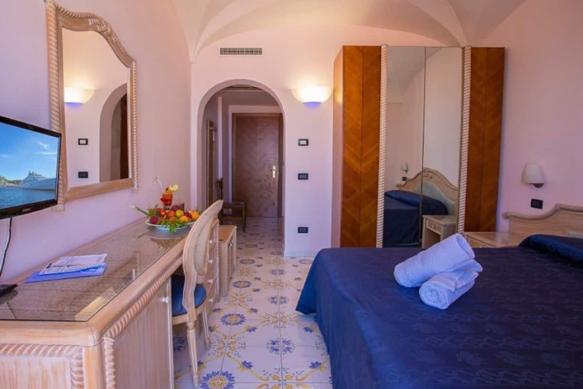 Habitación de hotel con cama, escritorio con computadora, espejo y vista al mar.