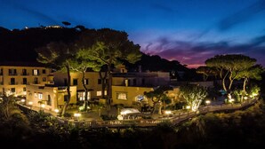 A nighttime view of a coastal town with illuminated buildings, a bridge, and trees. - Hotel Terme Cristallo Palace  (Casamicciola Terme)