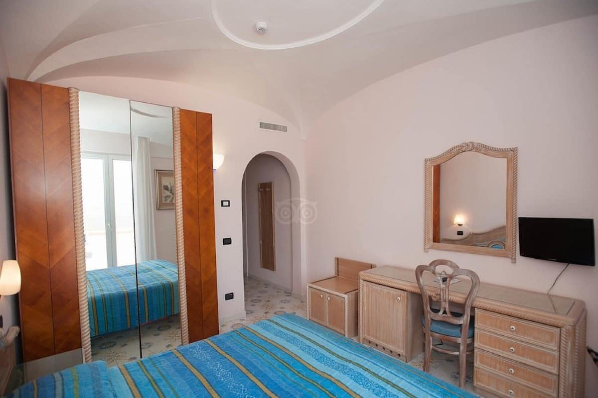 Un dormitorio con una cama, un tocador, una silla, un espejo y un televisor.