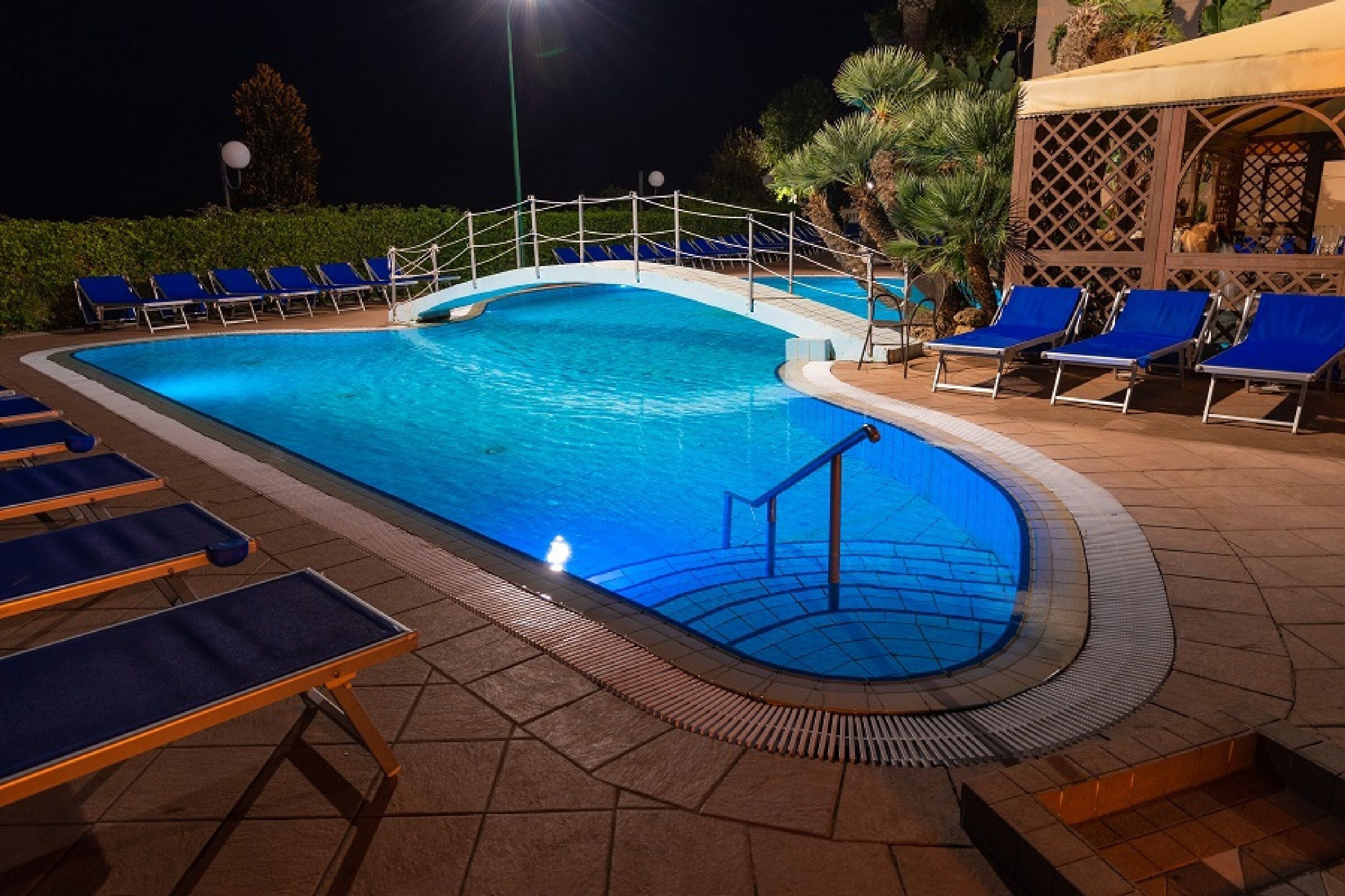 Una piscina con un pequeño puente, sillas de descanso y una zona de estar cubierta.
