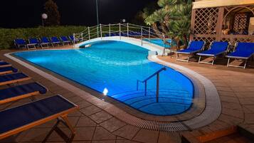 Una piscina con un pequeño puente, sillas de descanso y una zona de estar cubierta.