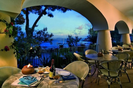 A table set with a bottle, glasses, and a book, overlooking a body of water with boats.. Hotel Terme Cristallo Palace