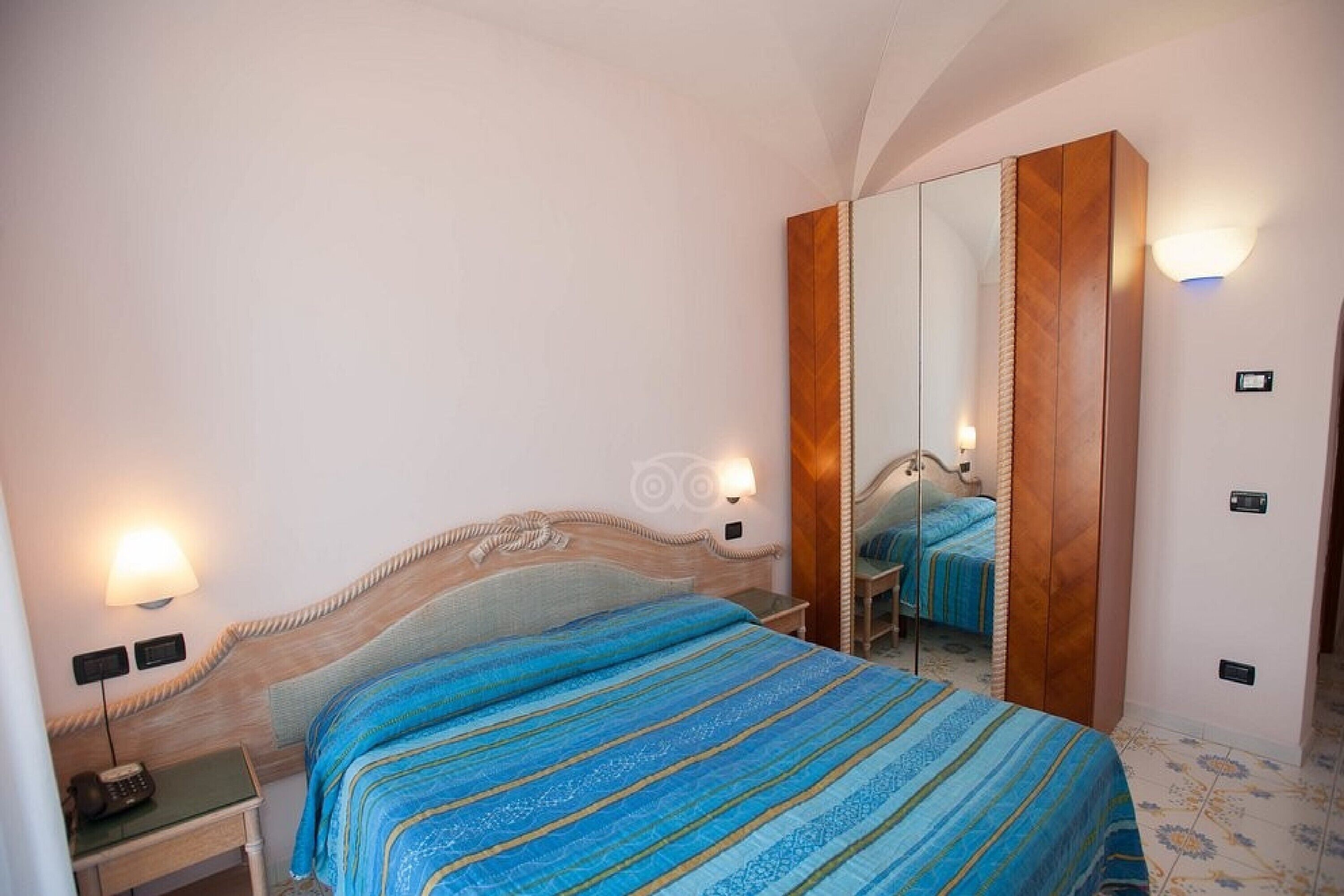 A hotel room with a bed, bedside lamps, a nightstand, a mirror, and a wardrobe.