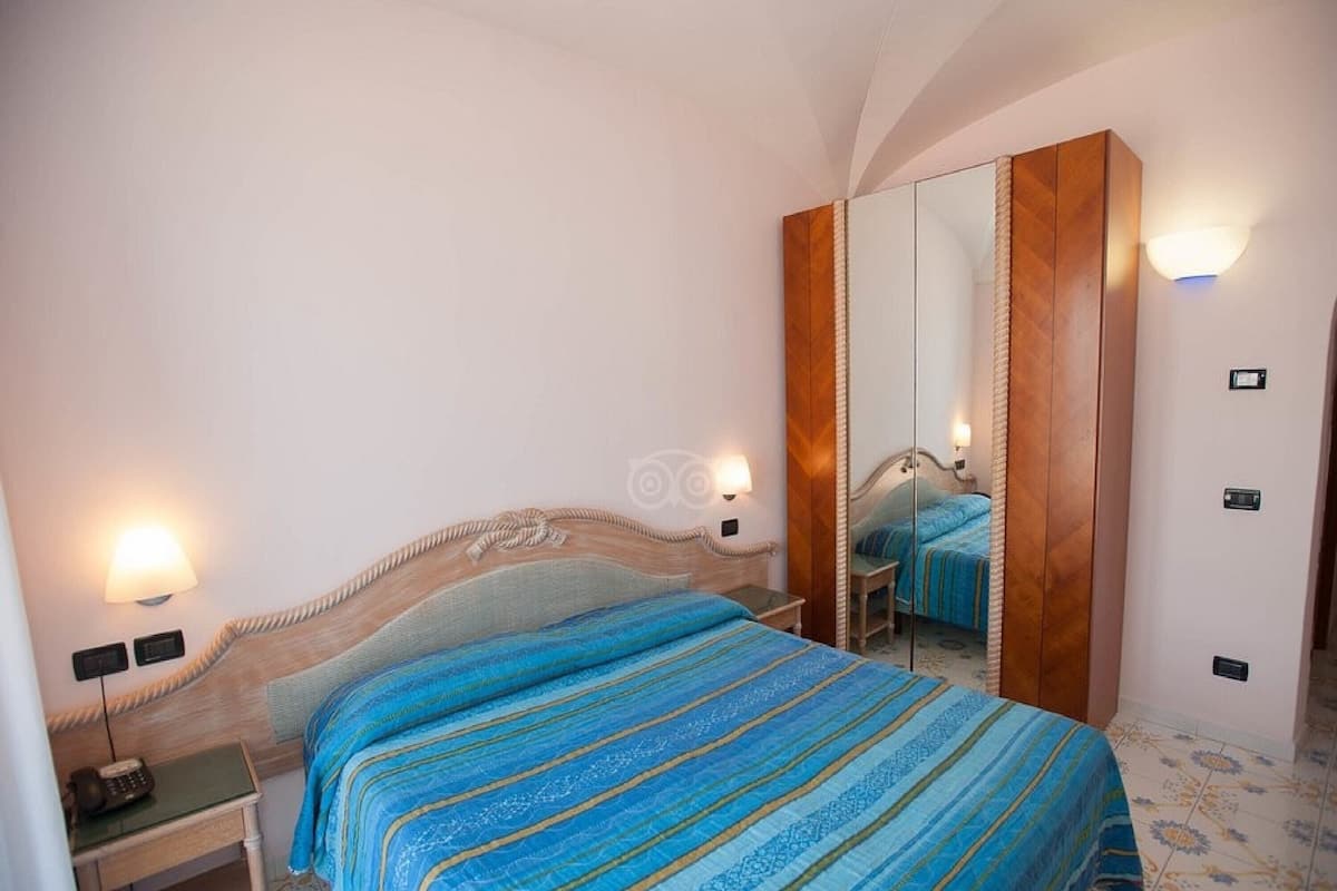 Una habitación de hotel con cama, lámparas de noche, mesita de noche, espejo y armario.