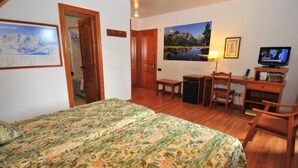 Une chambre à coucher avec un lit, un bureau, une chaise, un téléviseur et un tableau accroché au mur.