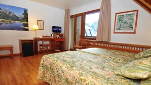 Une chambre d’hôtel équipée d’un lit, d’un bureau, d’une chaise, d’une télévision et ornée d’un tableau représentant un paysage de montagne.