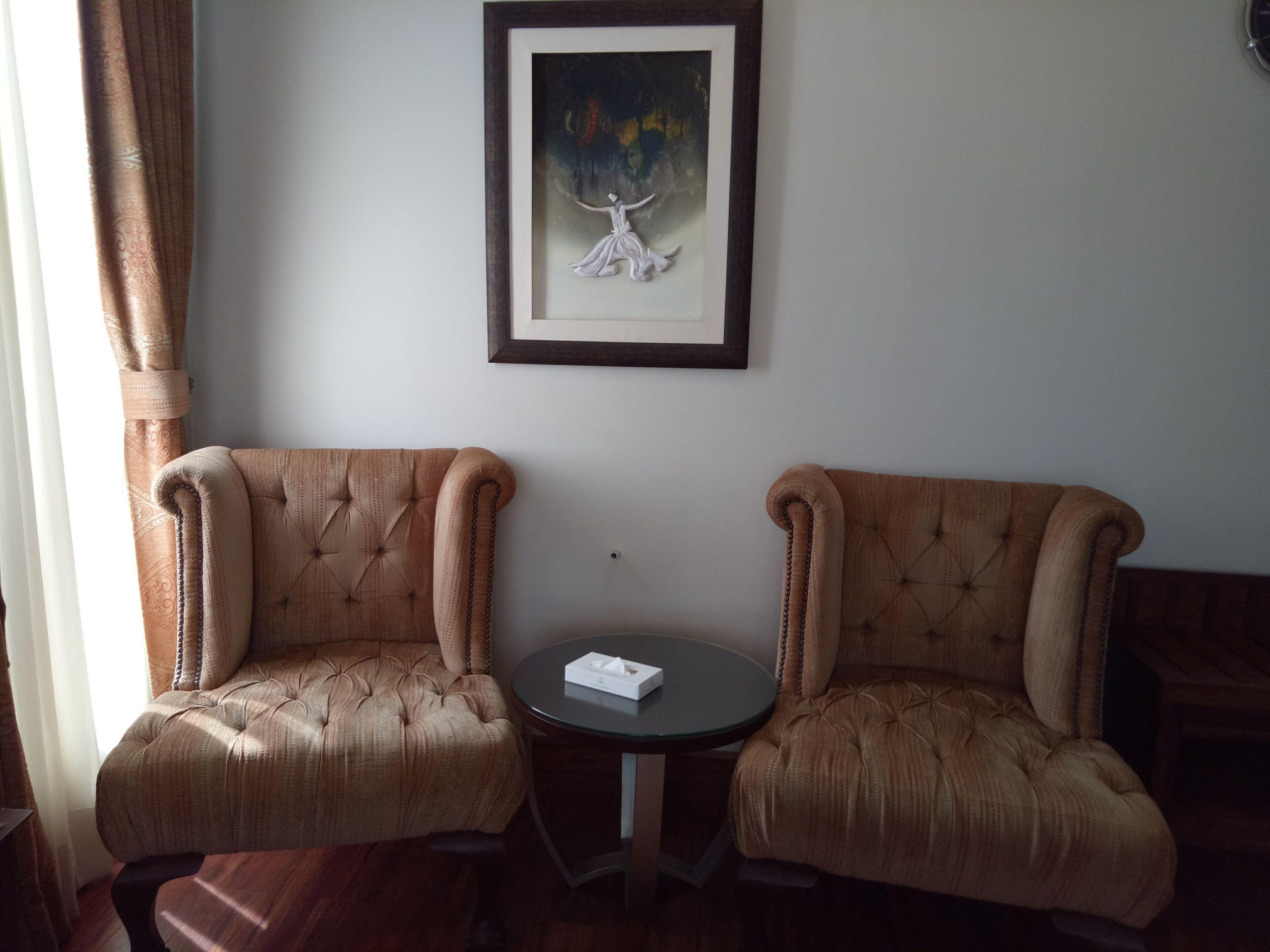 Une pièce comprenant deux fauteuils rembourrés, une petite table ronde et une œuvre d’art encadrée accrochée au mur.