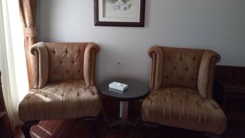 Une pièce comprenant deux fauteuils rembourrés, une petite table ronde et une œuvre d’art encadrée accrochée au mur.