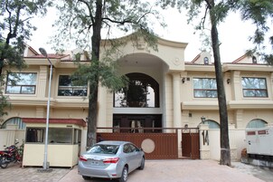 Un edificio grande de dos pisos con fachada color beige, un arco central y una entrada con portones.