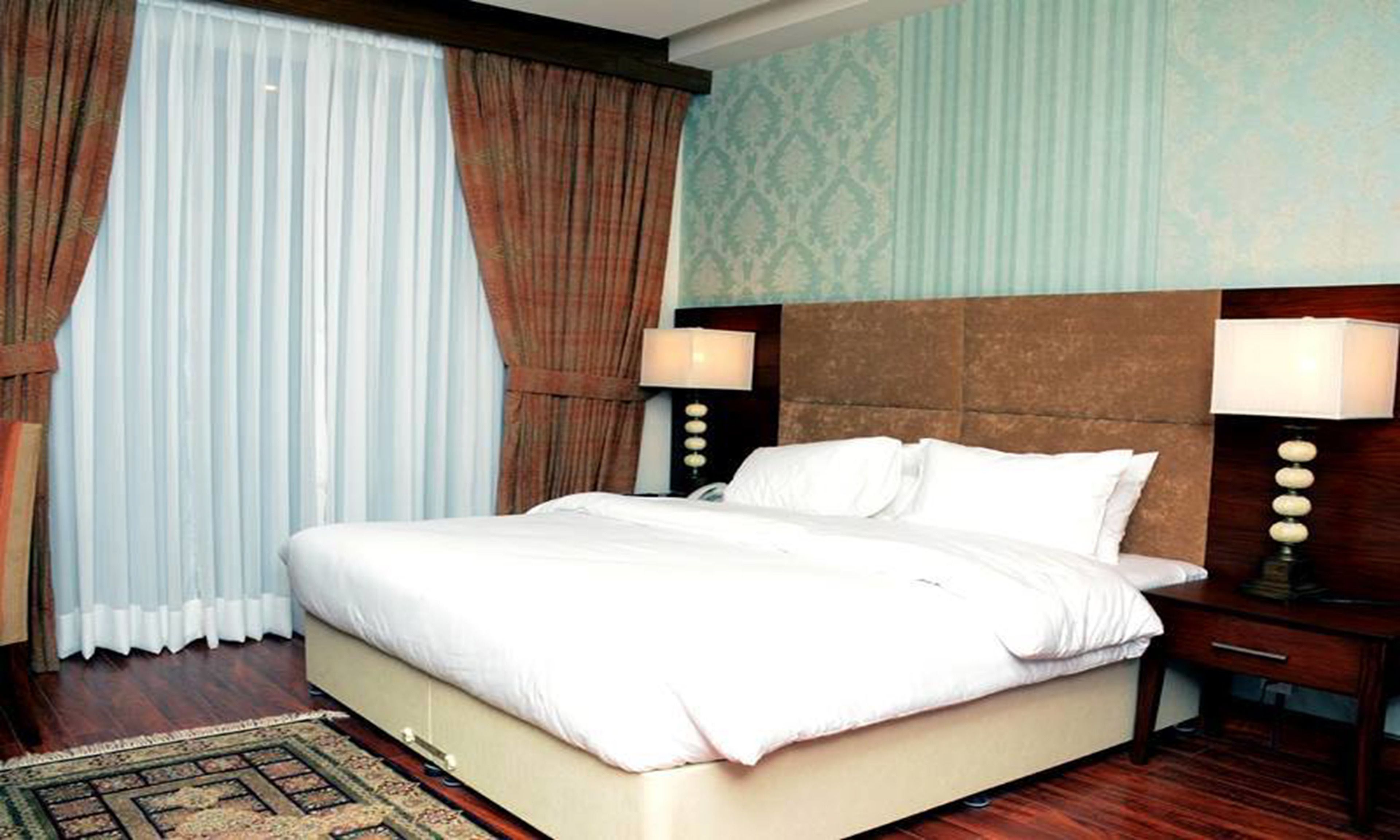 A hotel room with a large bed, two bedside lamps, a wooden headboard, and a patterned wall.