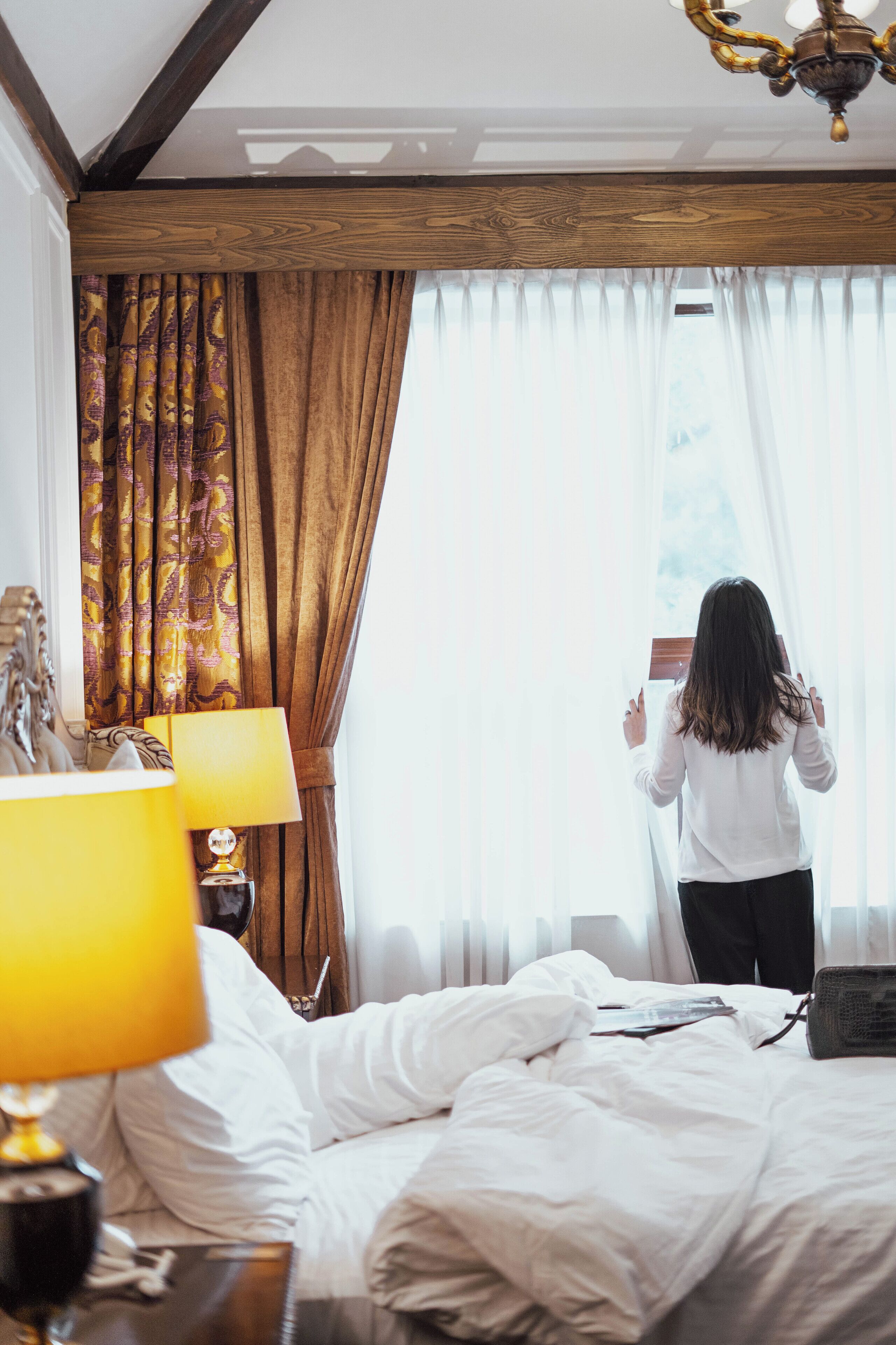 A hotel room with a bed, a nightstand with a lamp, and a window with curtains.