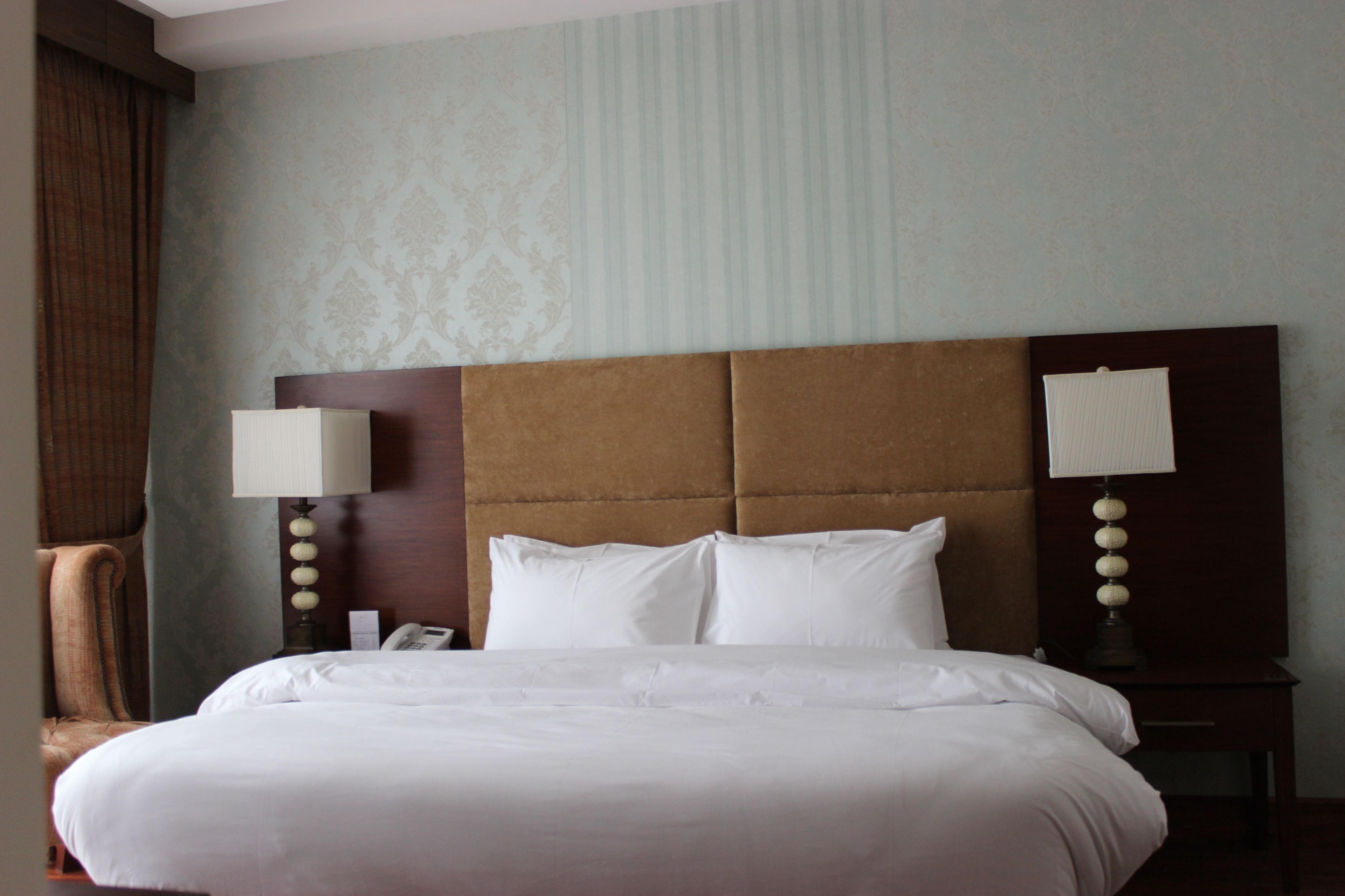 Una habitación de hotel con una cama grande, dos mesitas de noche con lámparas, una silla y una pared con diseño.