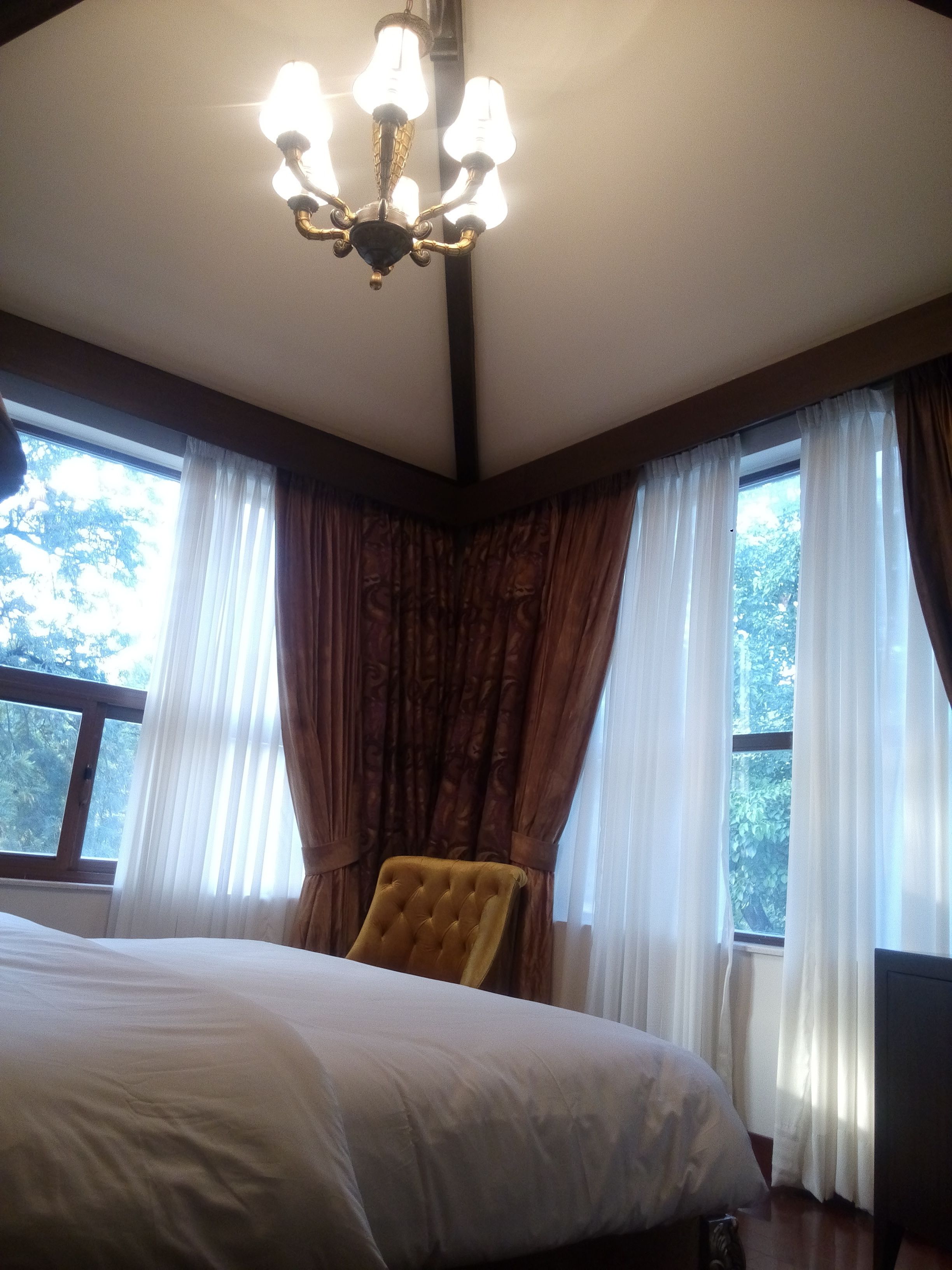 A bedroom with a large bed, a chandelier, and curtains on the windows.