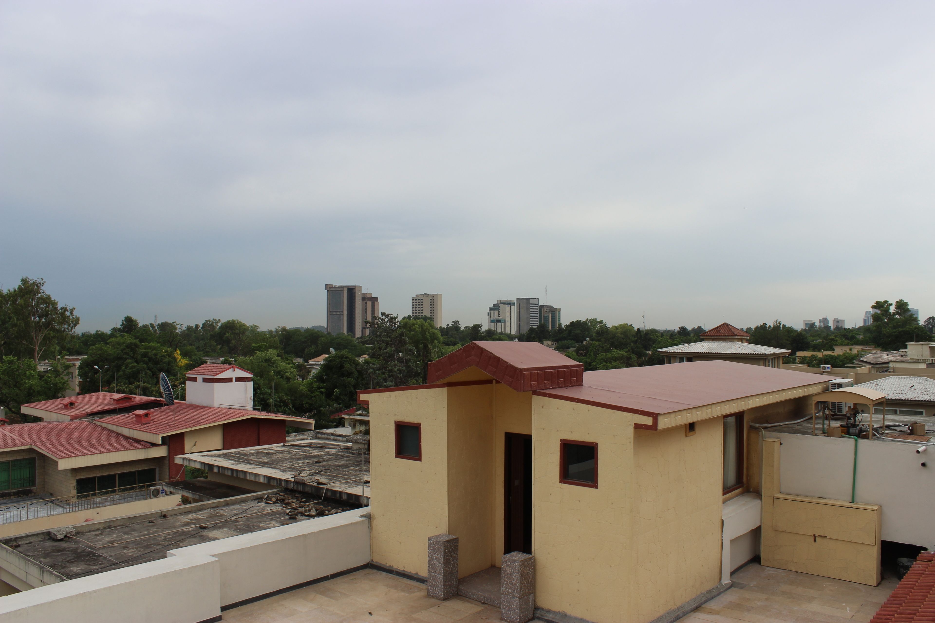 A rooftop with a small building, a satellite dish, and a view of surrounding buildings and trees.