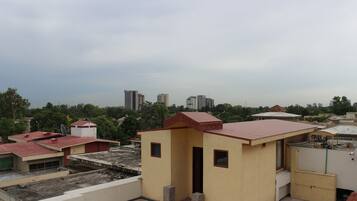 A rooftop with a small building, a satellite dish, and a view of surrounding buildings and trees.