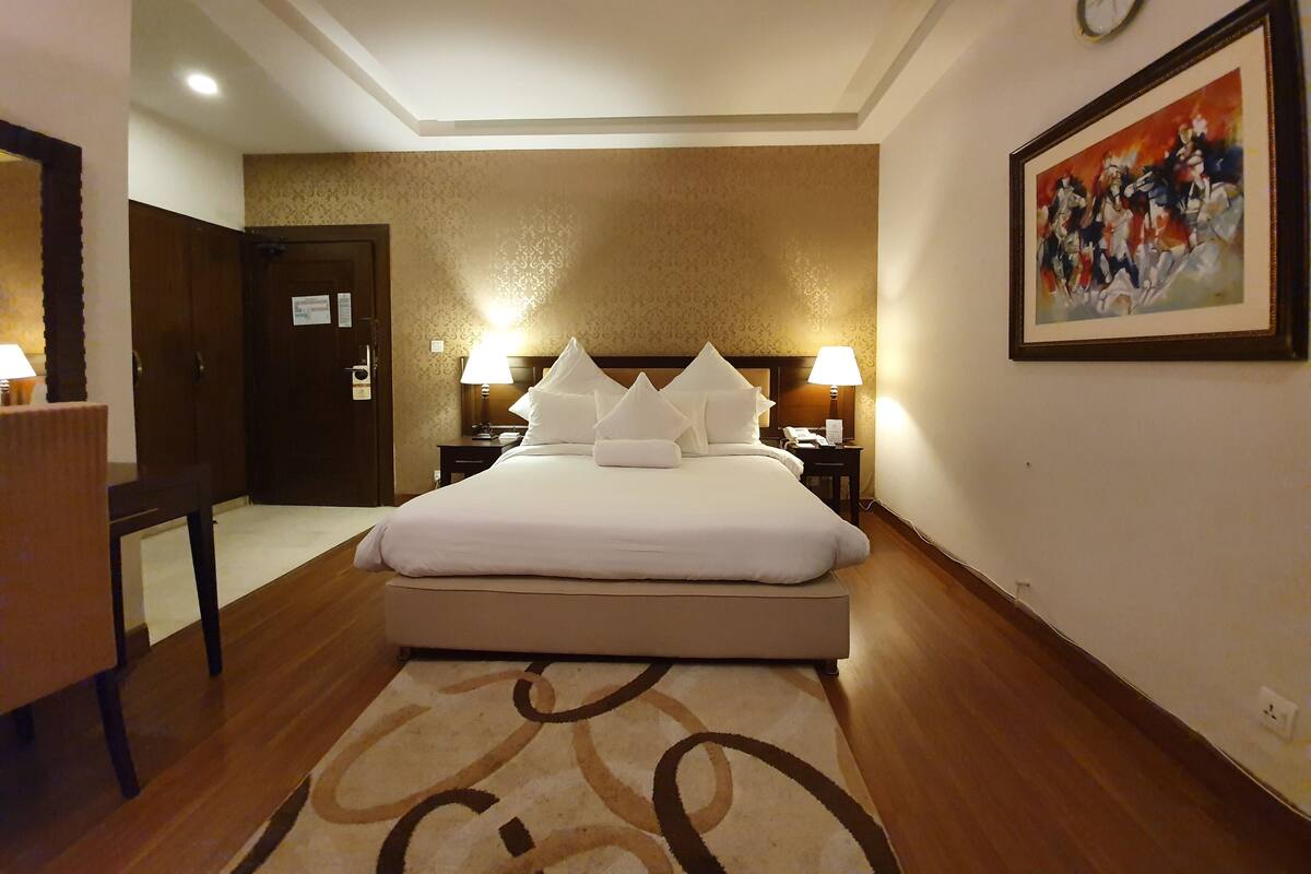 Habitación de hotel con una cama grande, dos lámparas de noche, un reloj en la pared y un cuadro.