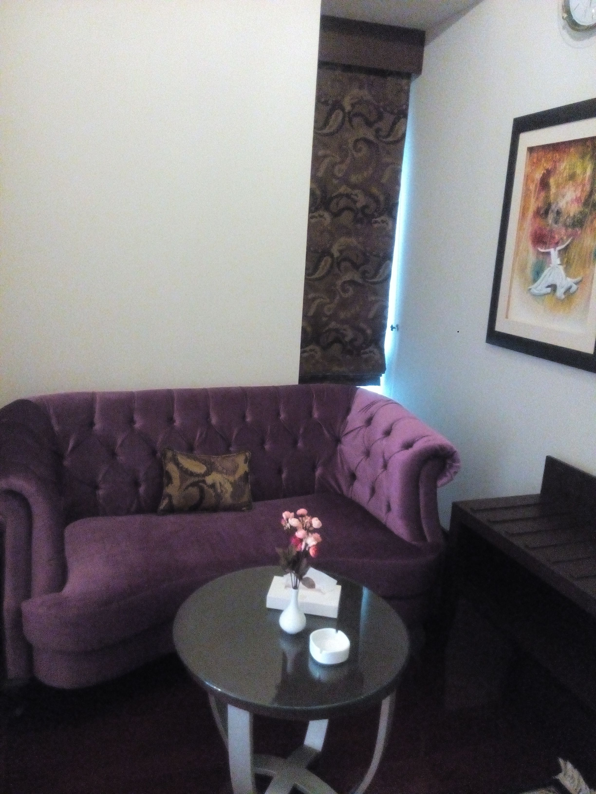 A purple sofa with a cushion, a small round table with a vase and a tissue box, and a framed picture on the wall.