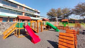 A playground with multiple slides and climbing structures, set against a building with a stone facade and multiple windows. - Hotel Surya Indah (Batu)