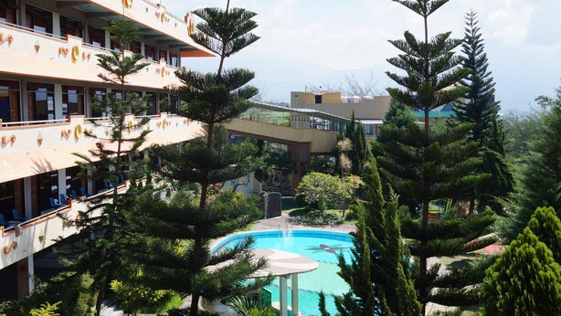 A hotel with multiple floors, outdoor swimming pool, and lush greenery. - Hotel Surya Indah (Batu)