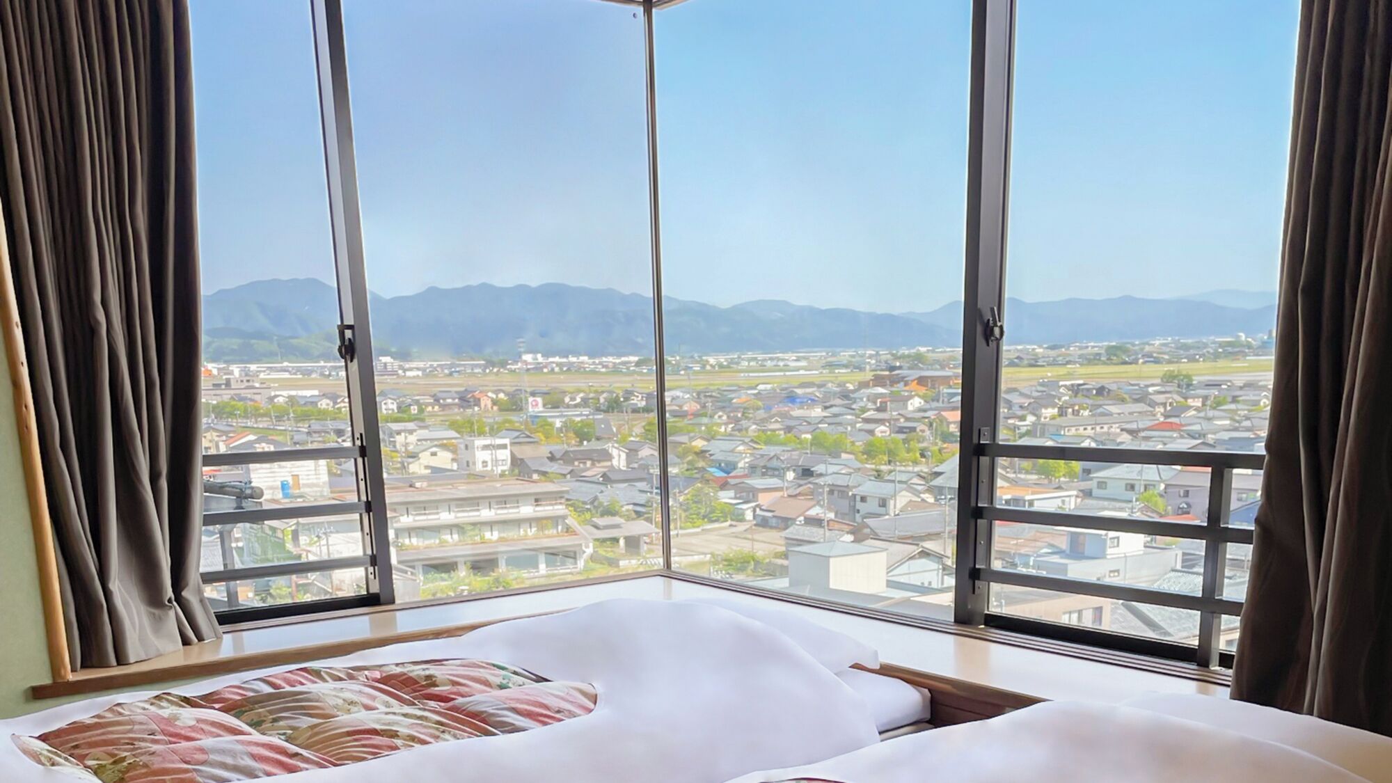 A hotel room with a large window, a bed, and a view of a town and mountains.