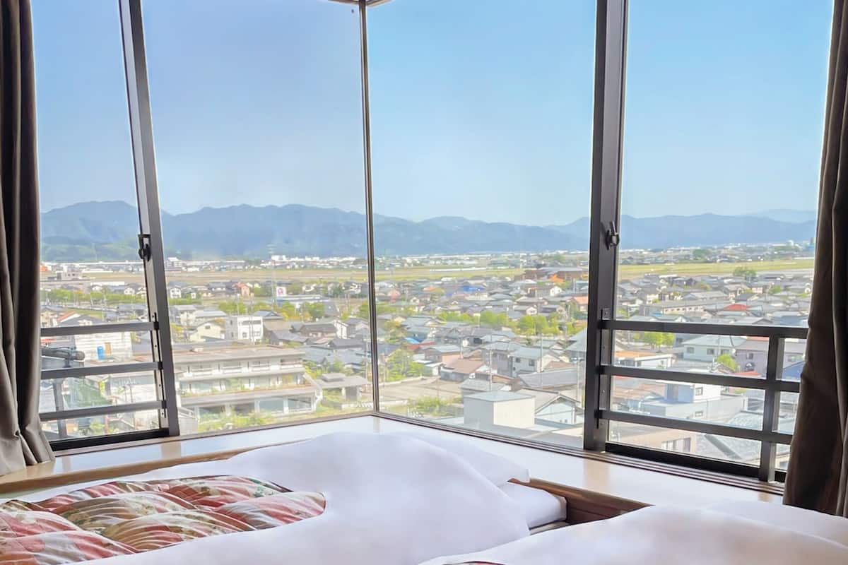 A hotel room with a large window, a bed, and a view of a town and mountains.