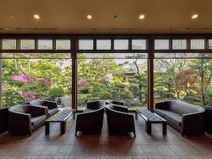 A room with a view of a garden, featuring wicker furniture and a tiled floor.