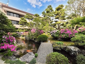 A traditional Japanese garden with a koi pond, stone pathway, and various flowering plants.