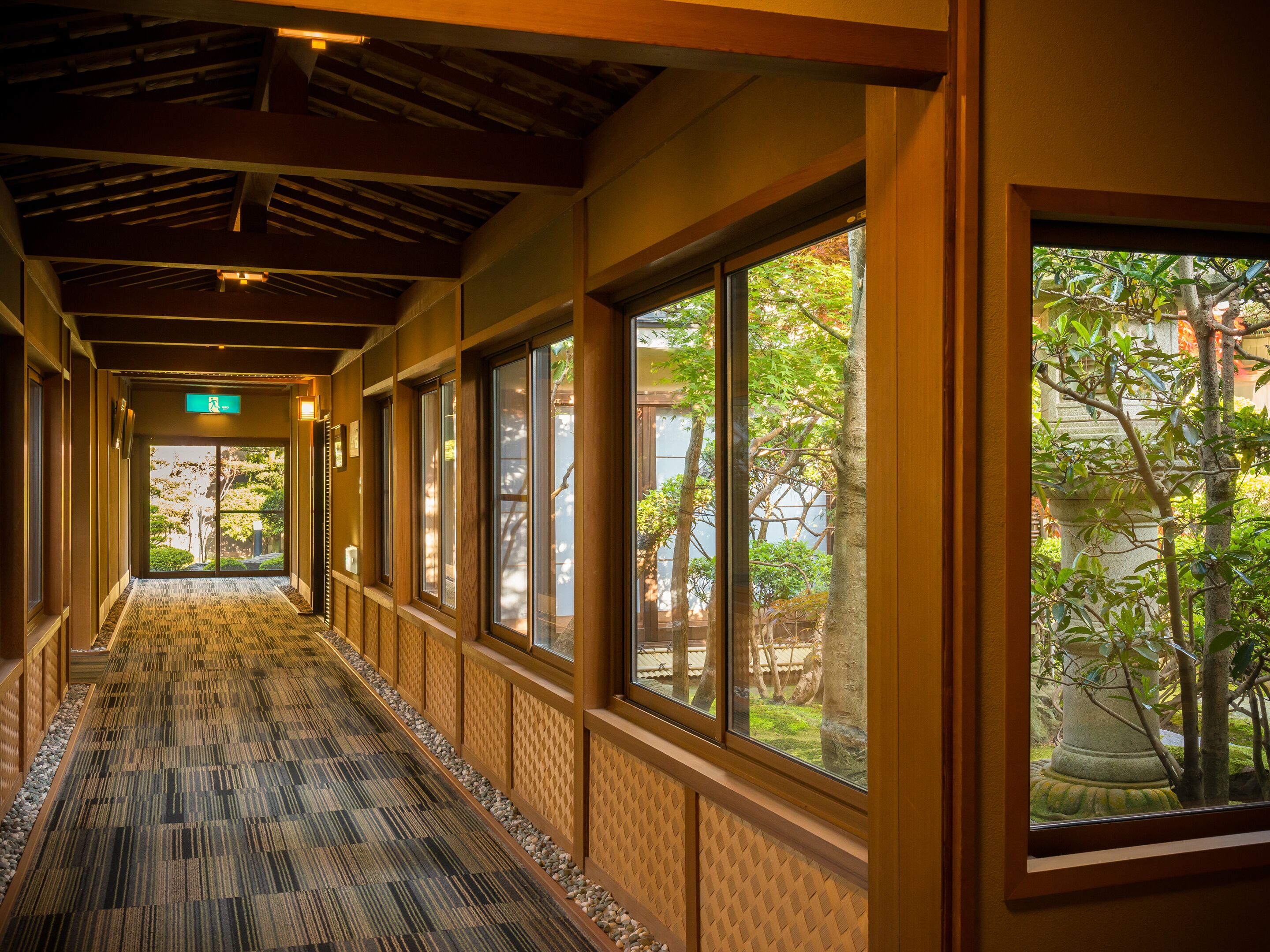A corridor with patterned carpet, large windows, and a view of greenery outside.