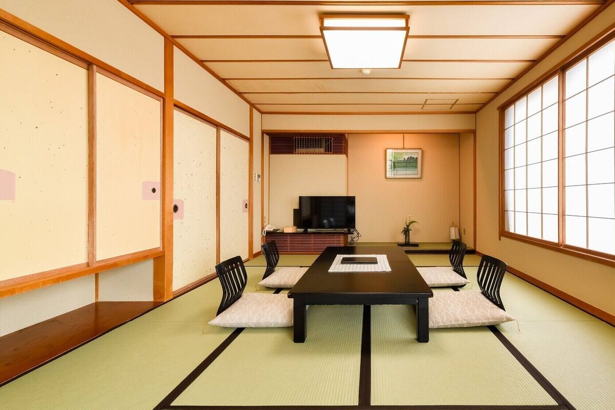 A traditional Japanese room with tatami flooring, a low table, black chairs, a television, and sliding doors.
