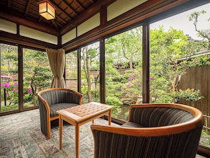 A room with large windows, a wooden ceiling, and a view of a garden with trees and a pond.
