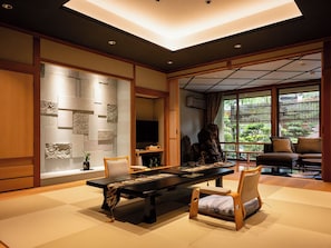 Ein traditioneller japanischer Raum mit Tatami-Boden, einem niedrigen Tisch und Blick auf einen Garten durch große Fenster.