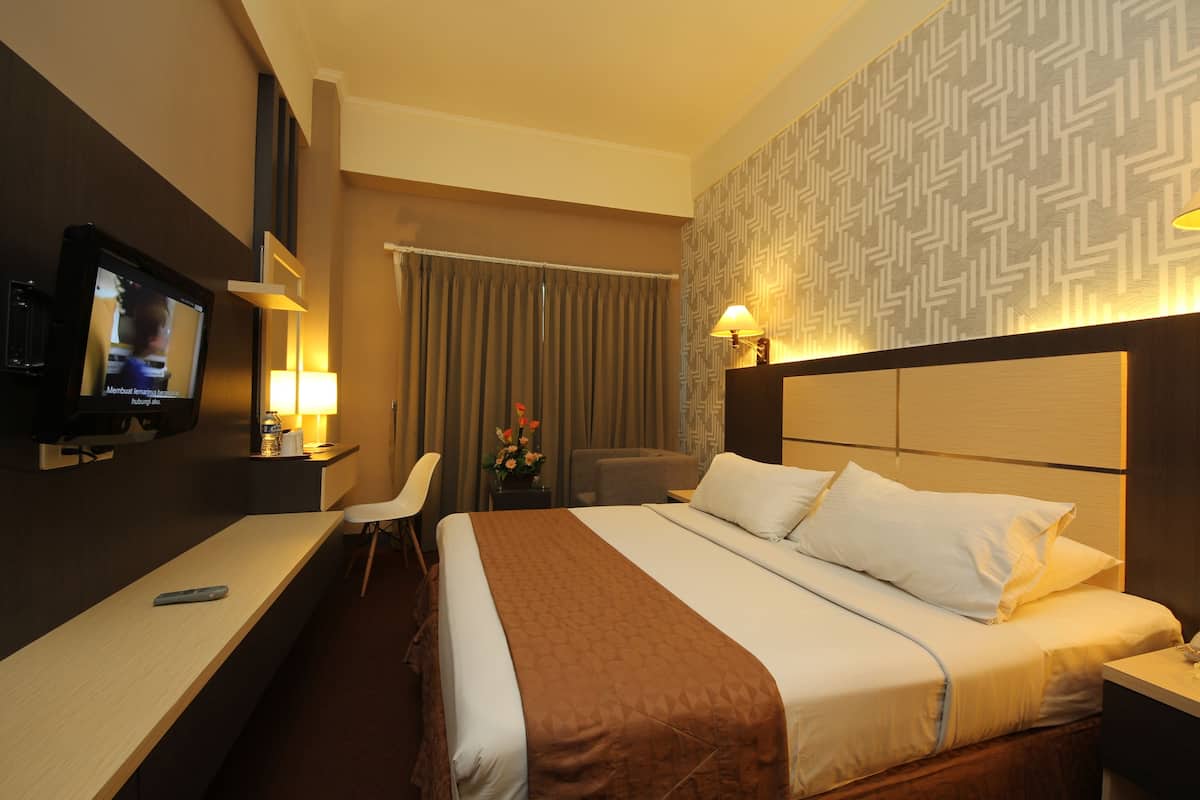 A hotel room with a bed, a desk with a TV, a chair, and a lamp.
