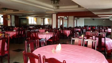 A large banquet hall with multiple round tables covered in pink tablecloths and wooden chairs.