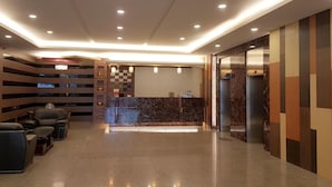 Een moderne hotellobby met een receptiebalie, zithoek en liften.