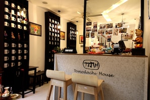 A reception area with a 'Tomodachi House' sign, shelves with mugs, a statue, and a 'Tour Desk'. - Tomodachi House (Hanoi)