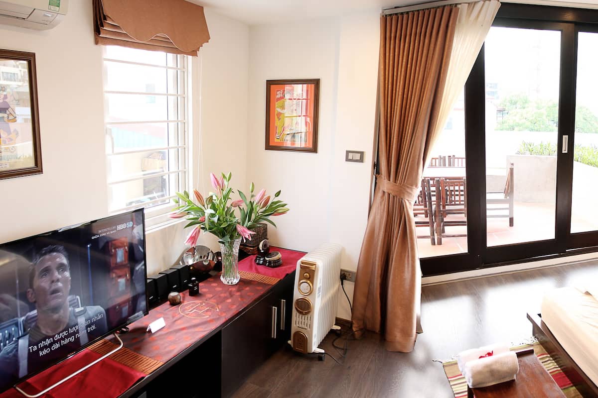 A hotel room with a television, a desk with a vase of flowers, a bed, and a sliding glass door to the outside.