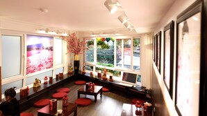 A room with a wooden floor, red seating, a large window with a view, and a white desk with a computer. - Tomodachi House (Hanoi)
