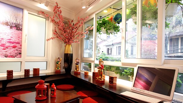A room with a wooden table, red cushions, a laptop, and decorative items including a vase and figurines. - Tomodachi House (Hanoi)