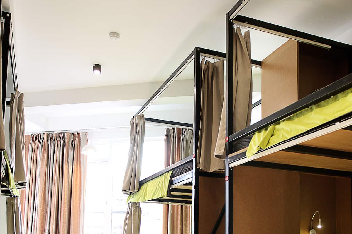 A bunk bed room with a window, curtains, and a bedside lamp.