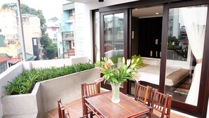 A balcony with a wooden table and chairs, a vase with flowers, and a view of the cityscape. - Tomodachi House (Hanoi)