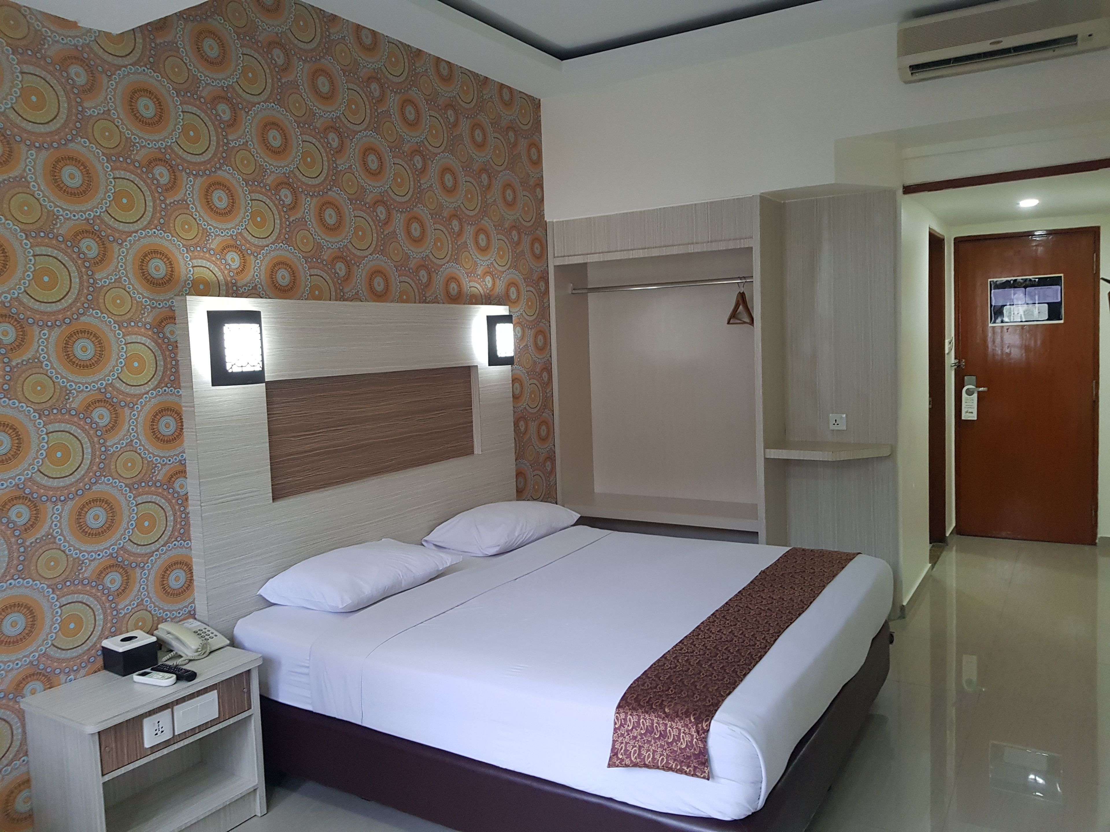 A hotel room with a bed, bedside table, and a wardrobe.