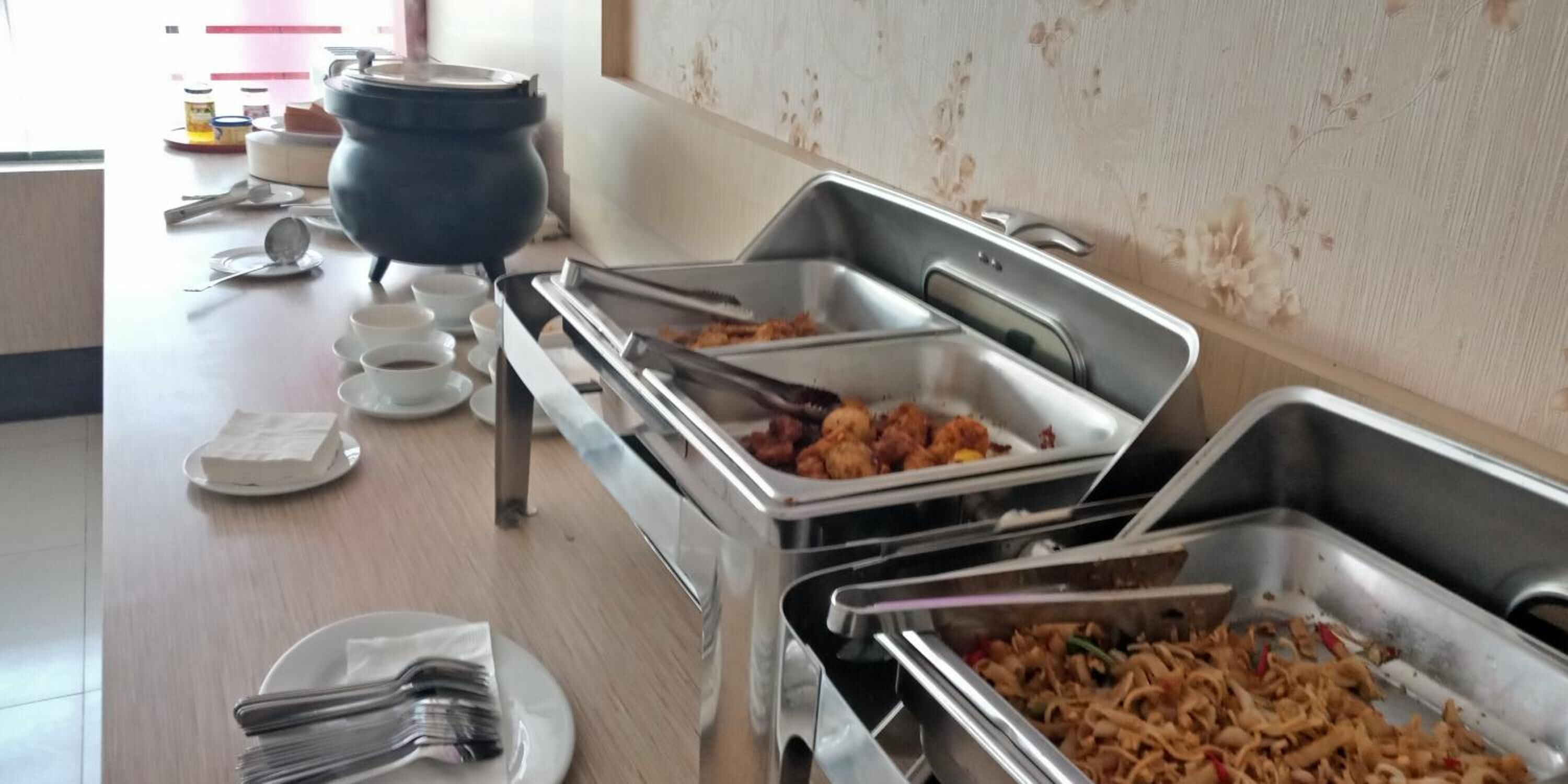 A buffet setup with various dishes, including fried items and noodles, and a large pot on the left.