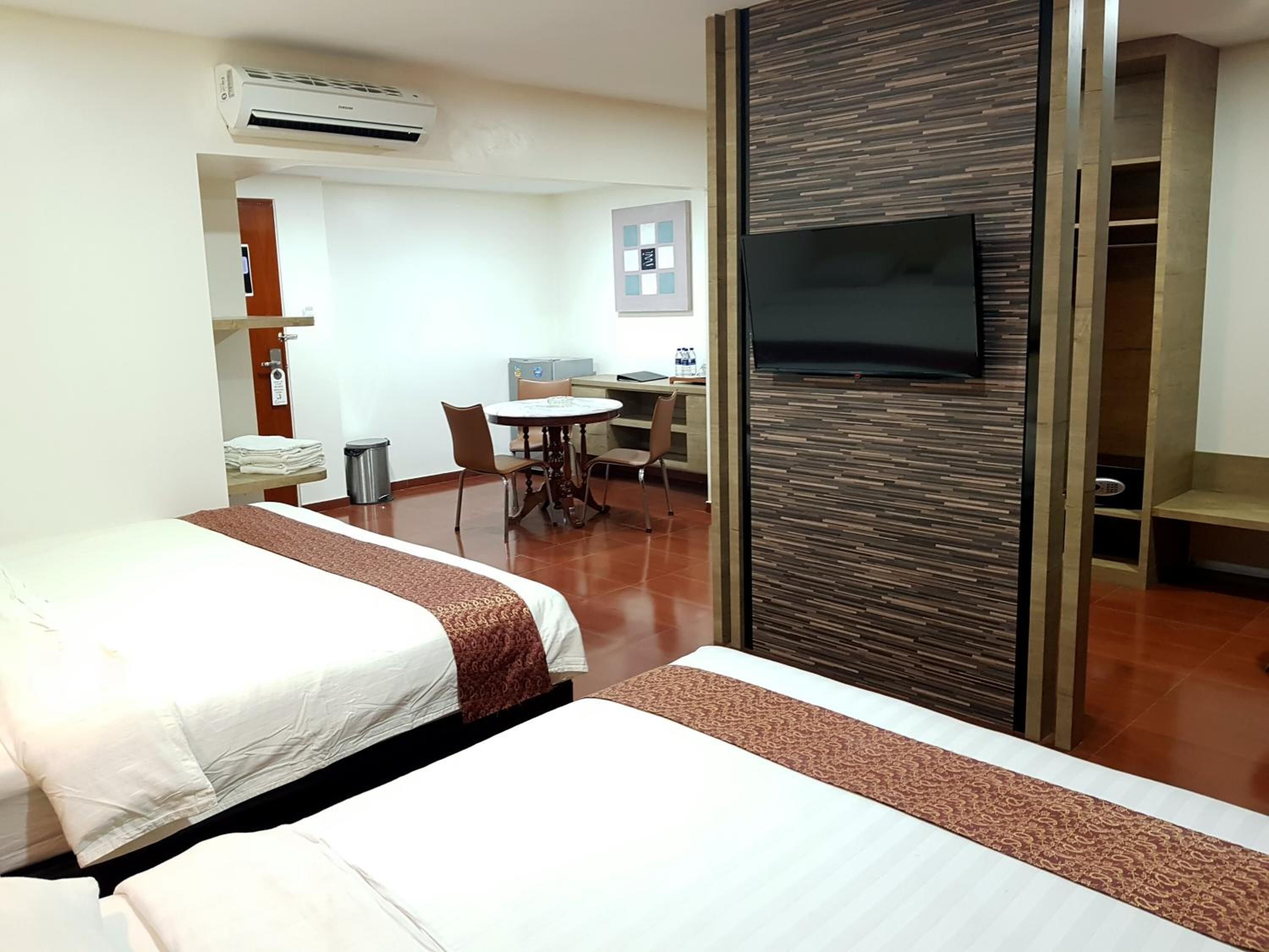 A hotel room with two beds, a desk, a chair, a TV, and a wardrobe.