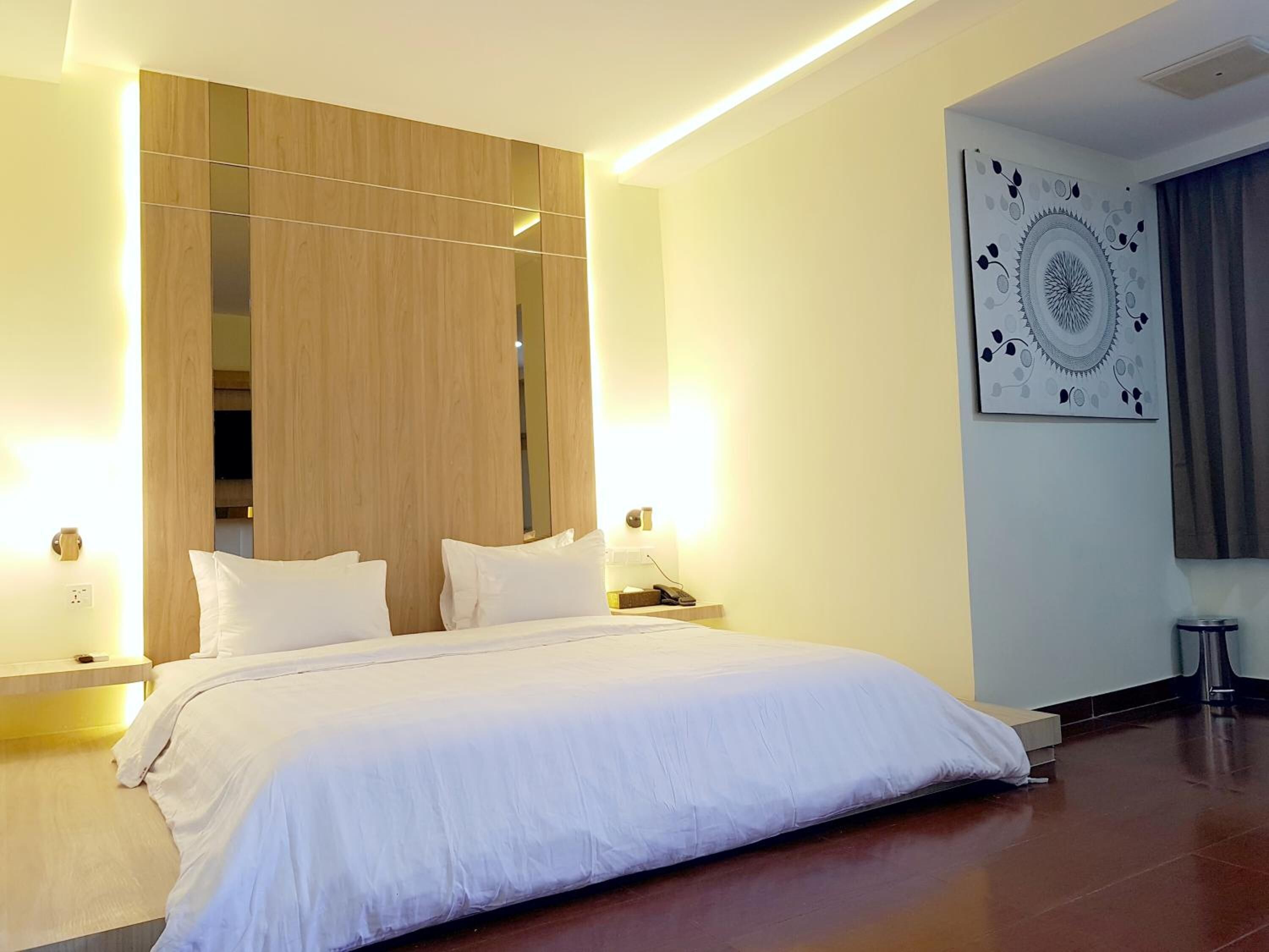 A hotel room with a large bed, wooden paneling, a wall-mounted mirror, a nightstand with a phone, and a decorative wall piece.