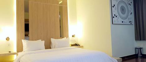 A hotel room with a large bed, wooden paneling, a wall-mounted mirror, a nightstand with a phone, and a decorative wall piece.