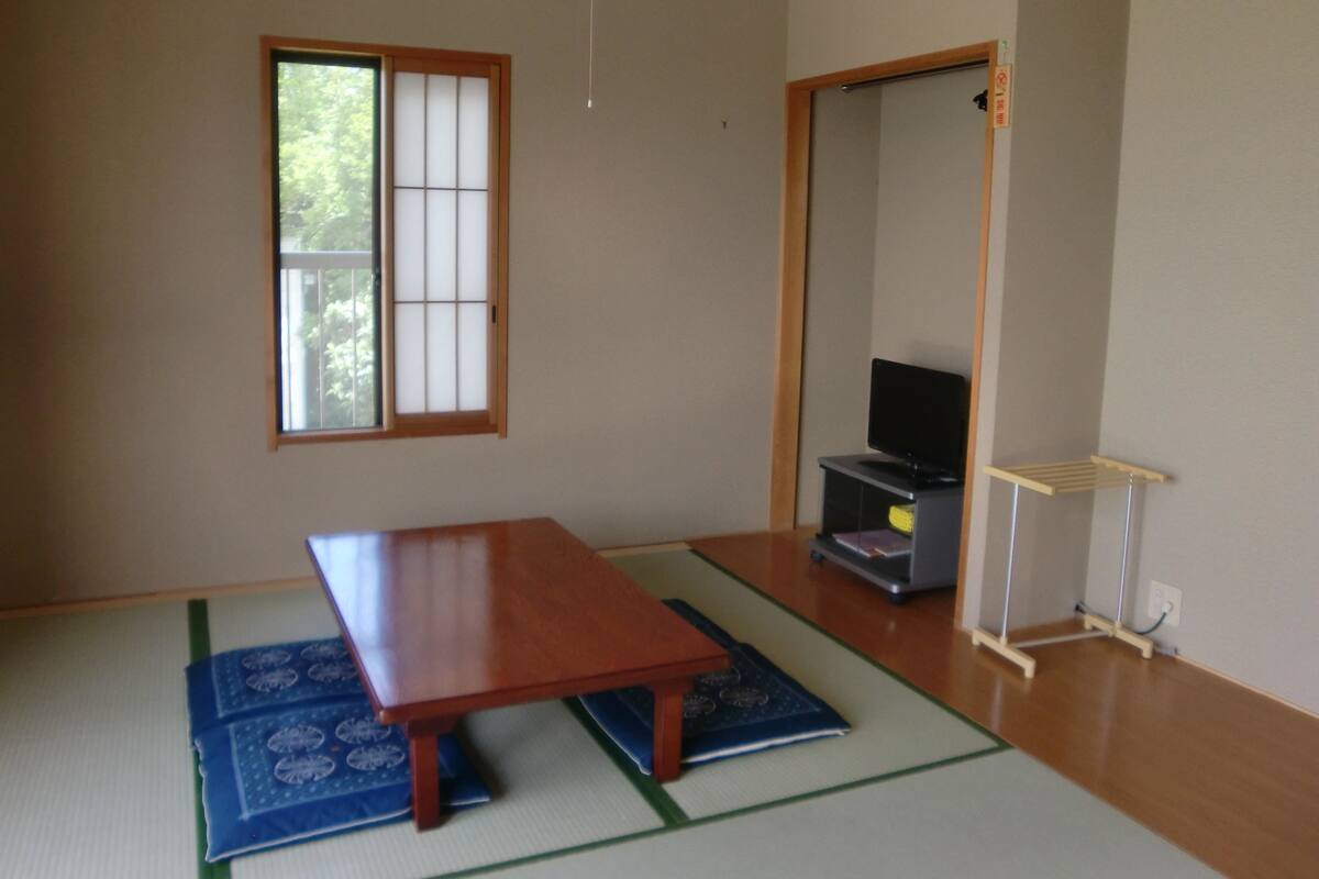 A room with tatami mats, a low wooden table, a television on a stand, and a sliding door.
