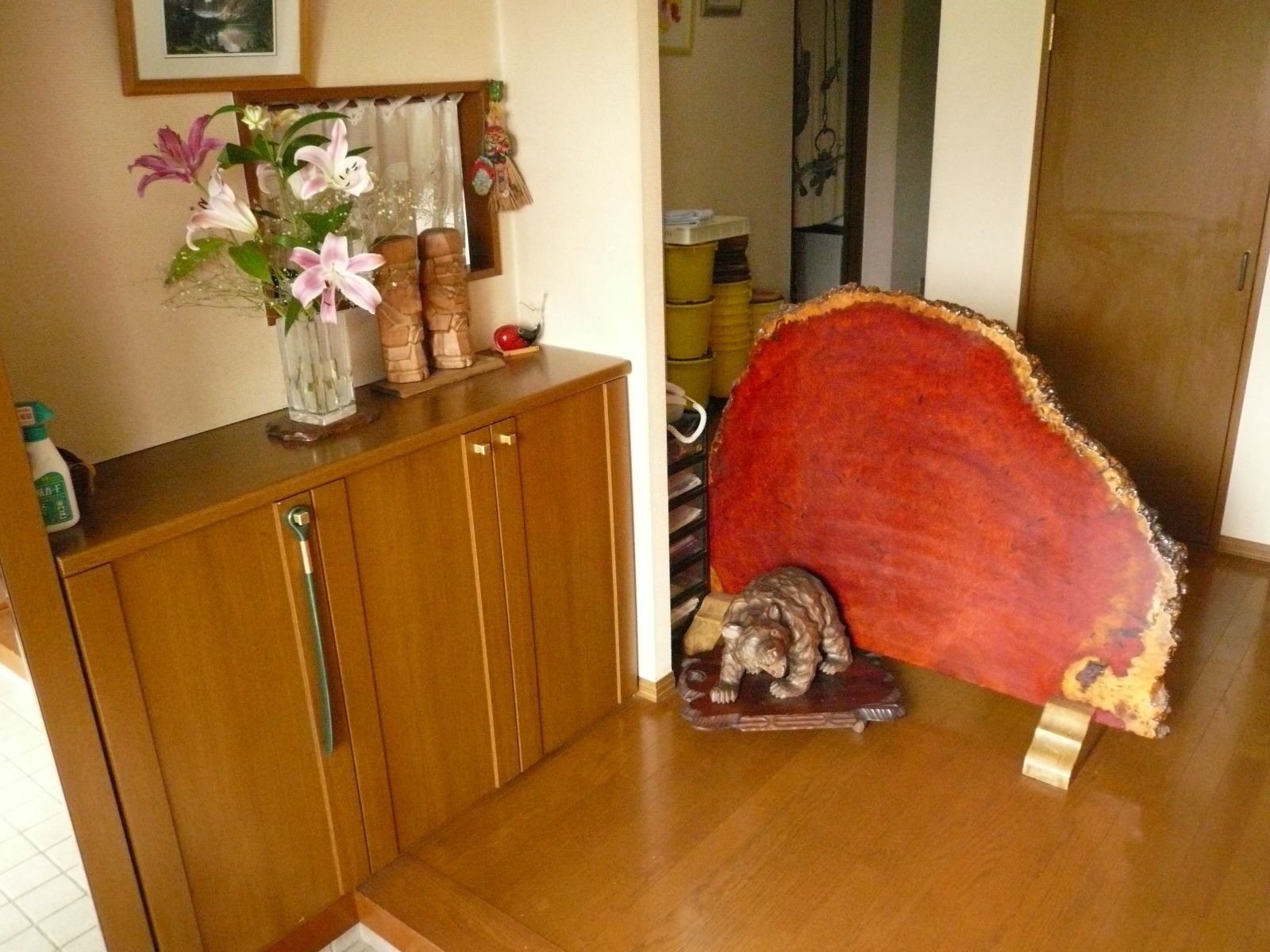 A wooden cabinet with a vase of flowers, a red decorative piece, and a small statue on a table.